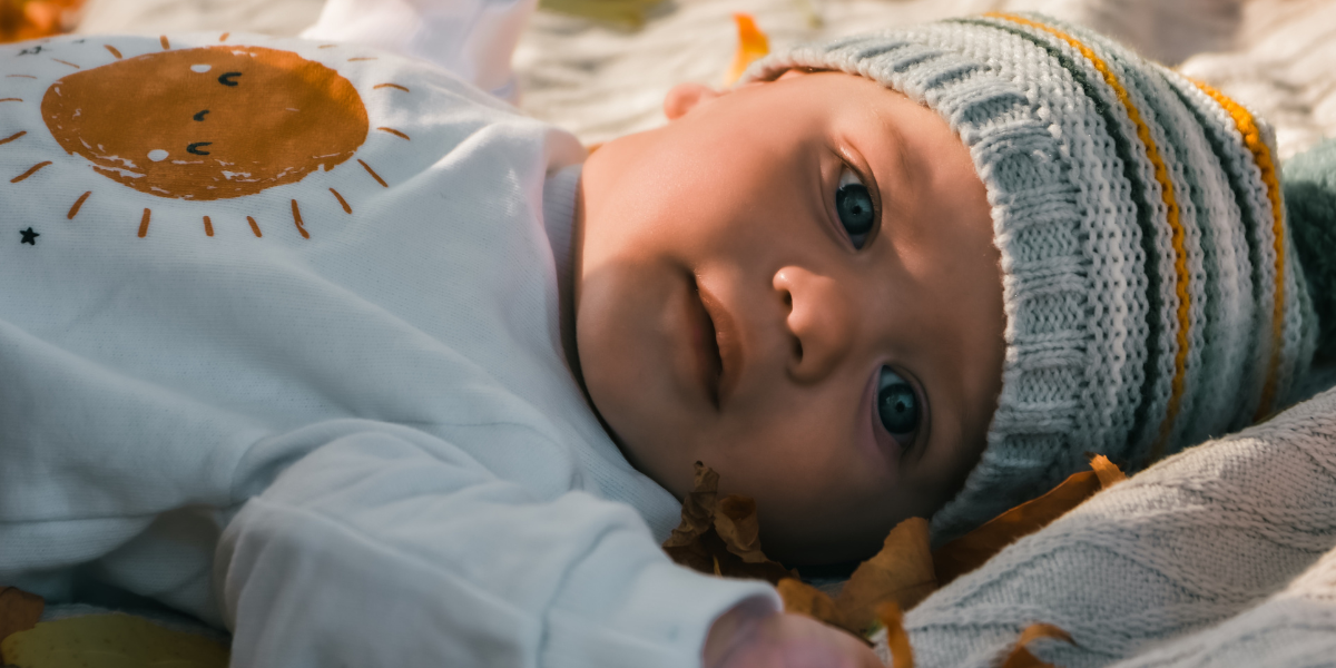 Cute baby with beanie on head wearing sun logo shirt looking to the left